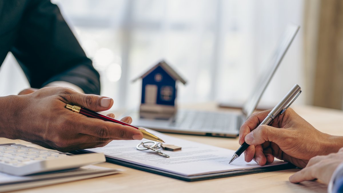 Two people reviewing and signing a home purchase contract beside a small model house and keys, illustrating real estate contract law